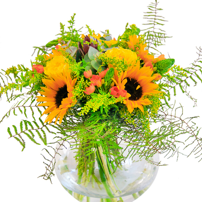 This uplifting bouquet, artfully created for Brent Cross, spills over with radiant colour and heartfelt craftsmanship in a gleaming round glass vase. Towering sunflowers, with plush yellow petals and dramatic brown centers, capture the essence of summer days spent along the Brent reservoir. Framing these, garden roses in buttery gold layers open with timeless elegance, their graceful spirals hinting at classic floral design. Glossy, berry-red Hypericum clusters pulse with energy amid a field of lush greenery: ferns and goldenrod provide gentle cascades and airy texture, as if caught in a soft breeze blowing through Clitterhouse Playing Fields. Blue-green eucalyptus leaves intersperse among the blooms, bringing a subtle depth and a refreshing scent. The transparency of the vase showcases the bouquet's sturdy stems, their crisscrossing angles revealing the meticulous artistry behind every arrangement delivered in Brent Cross. The bouquet is alive with textural interplay and vibrant tones, making it a striking centerpiece, a memorable gift for special occasions, or a conversation starter for gatherings by Prince Charles Drive. It embodies the natural charm of the area-inviting a sense of comfort, celebration, and fresh beginnings into every Brent Cross home.